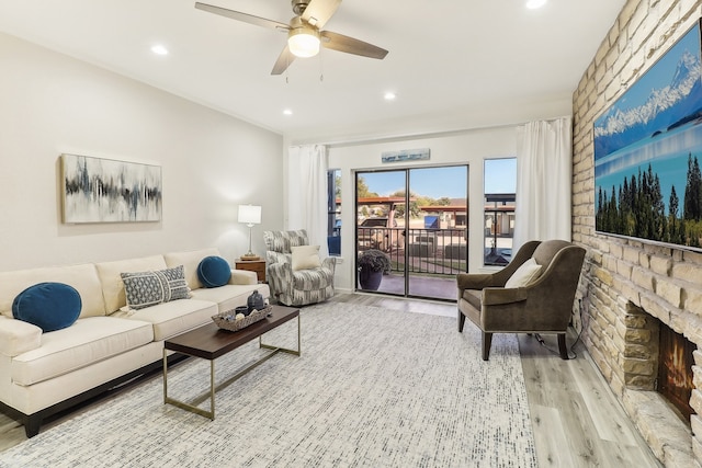 living room with light hardwood / wood-style floors, a stone fireplace, and ceiling fan