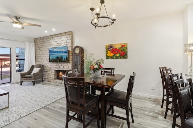 dining space with ornamental molding, light hardwood / wood-style flooring, a brick fireplace, and ceiling fan with notable chandelier