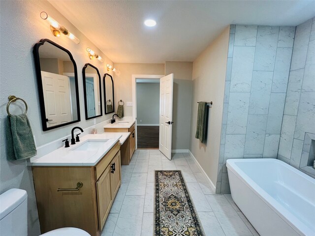 bathroom featuring tile patterned floors, a tub to relax in, toilet, vanity, and a textured ceiling