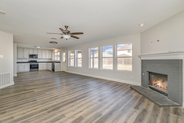 unfurnished living room with ceiling fan, a fireplace, sink, and light wood-type flooring