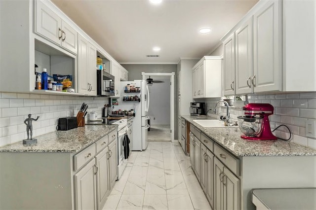 kitchen with white cabinets, light stone counters, backsplash, appliances with stainless steel finishes, and sink