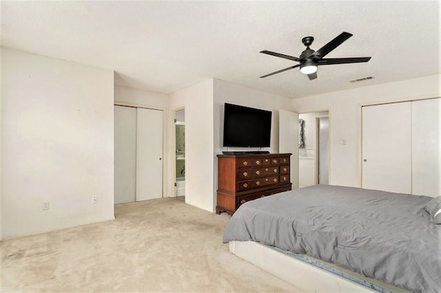 bedroom featuring two closets, light colored carpet, and ceiling fan