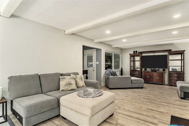 living room with a textured ceiling, beamed ceiling, and light wood-type flooring