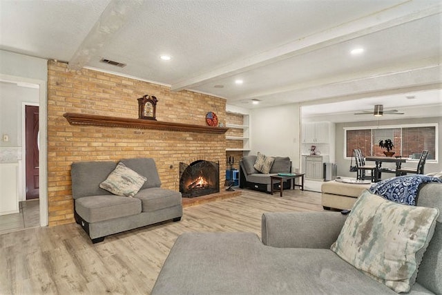 living room featuring light hardwood / wood-style flooring, a textured ceiling, beam ceiling, and a brick fireplace