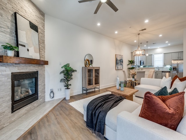 living room with a stone fireplace, ceiling fan, light hardwood / wood-style flooring, and sink