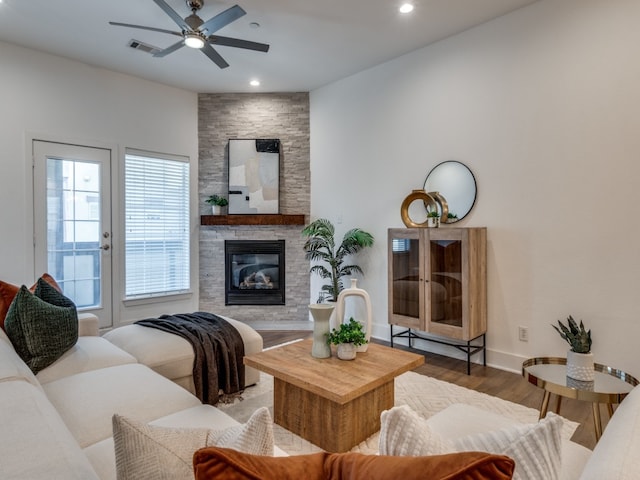 living room with ceiling fan, a stone fireplace, and wood-type flooring