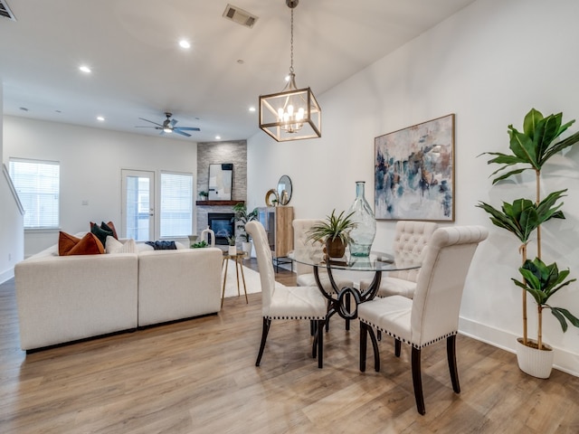 dining space with a stone fireplace, light hardwood / wood-style floors, and ceiling fan with notable chandelier