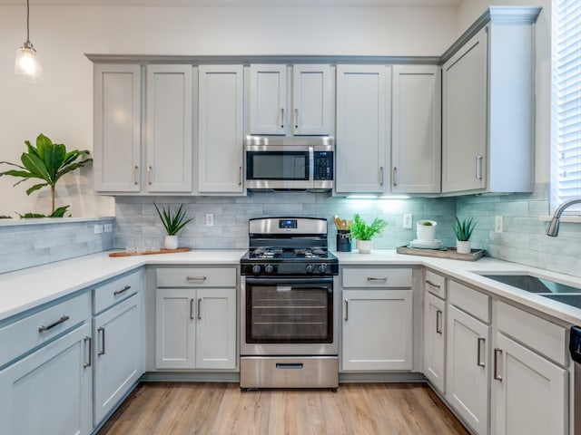 kitchen with light wood-type flooring, tasteful backsplash, stainless steel appliances, sink, and pendant lighting