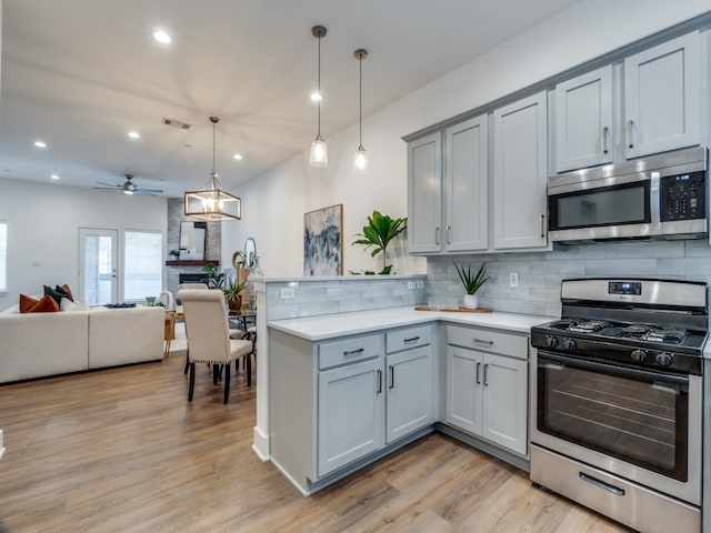 kitchen featuring gray cabinetry, hanging light fixtures, stainless steel appliances, a stone fireplace, and kitchen peninsula