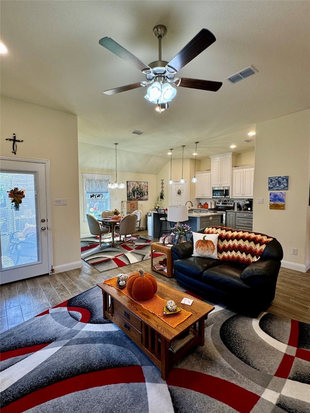 living room with light hardwood / wood-style floors, vaulted ceiling, and ceiling fan with notable chandelier