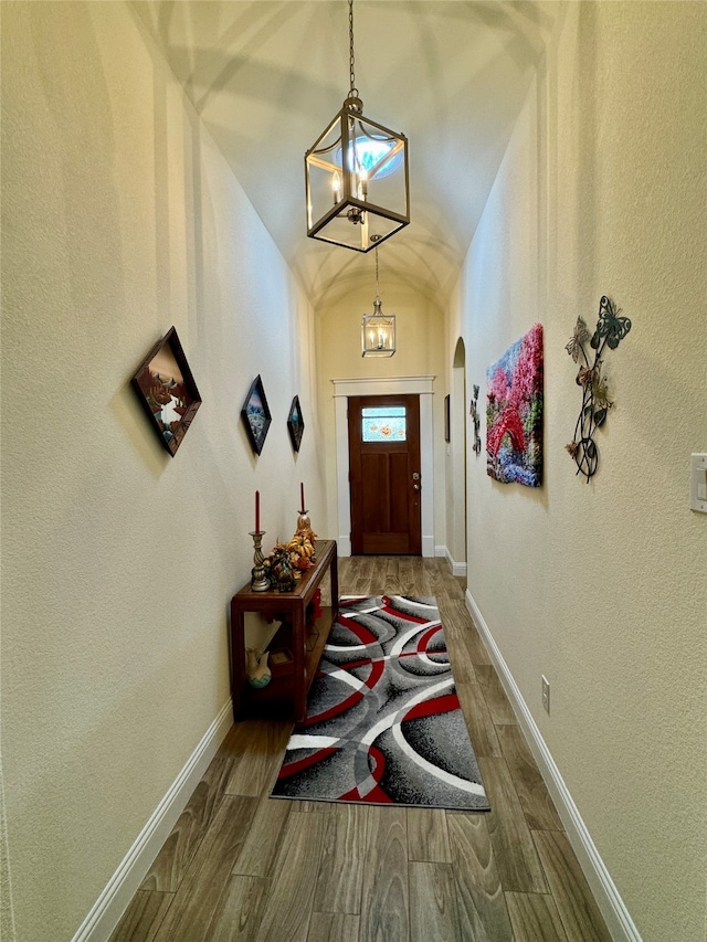 entryway with a notable chandelier, wood-type flooring, and vaulted ceiling