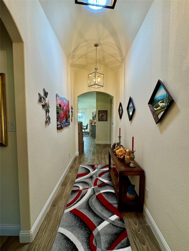 hall with a notable chandelier, dark wood-type flooring, and vaulted ceiling