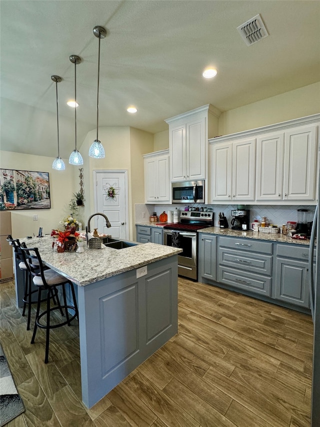 kitchen featuring an island with sink, stainless steel appliances, wood-type flooring, sink, and white cabinetry