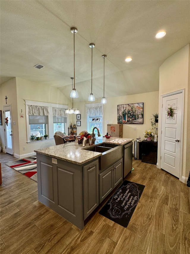 kitchen with lofted ceiling, dark hardwood / wood-style floors, an island with sink, gray cabinets, and light stone counters