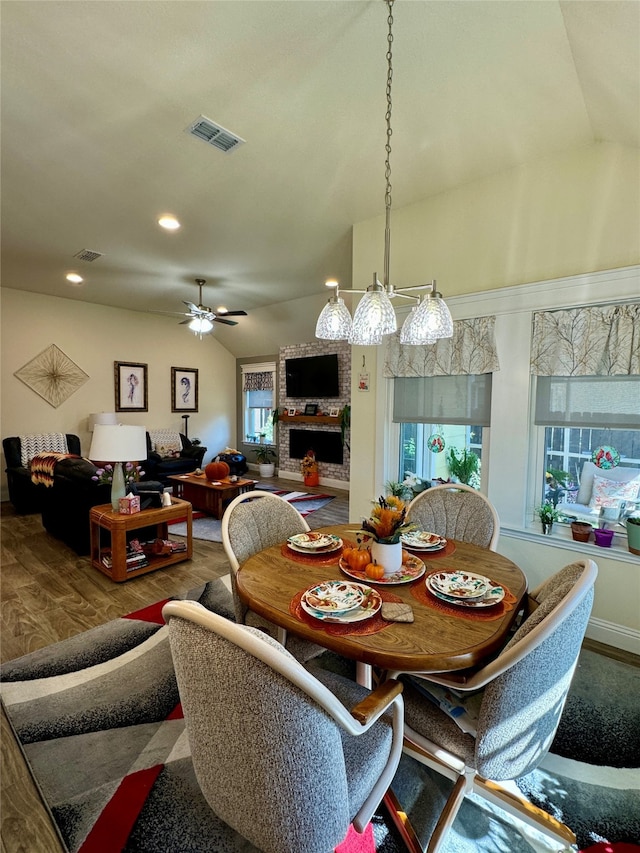 dining area with vaulted ceiling, a fireplace, wood-type flooring, and ceiling fan