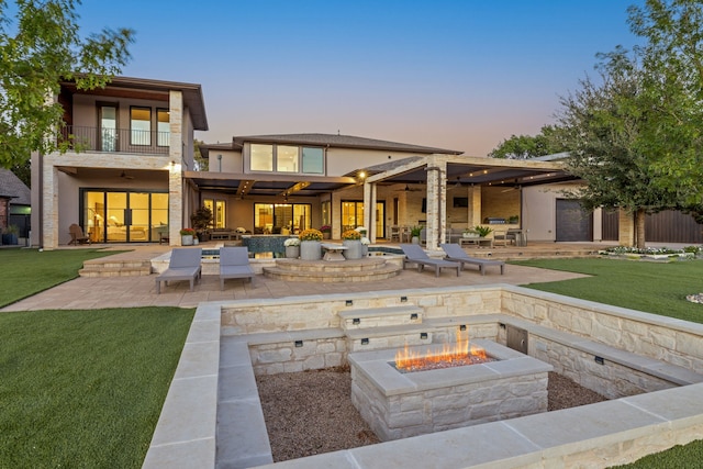 back house at dusk featuring a balcony, a yard, a patio area, and a fire pit