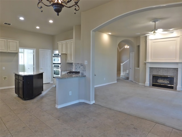 kitchen with ceiling fan, light stone countertops, light colored carpet, double oven, and a center island