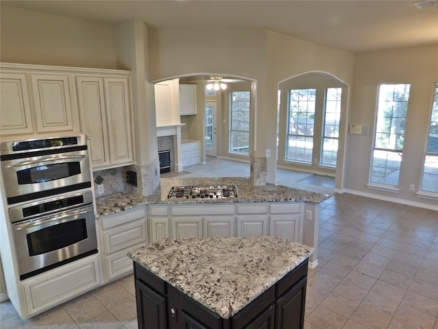 kitchen featuring white cabinets, a kitchen island, appliances with stainless steel finishes, ceiling fan, and light stone countertops