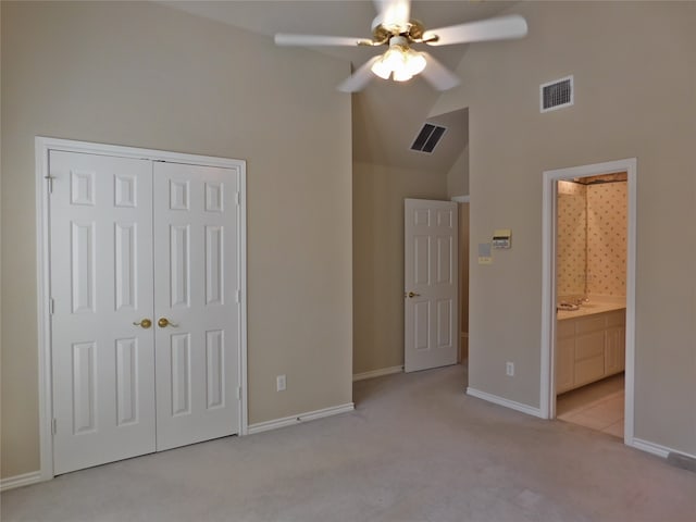 unfurnished bedroom with a closet, vaulted ceiling, light colored carpet, ensuite bathroom, and ceiling fan