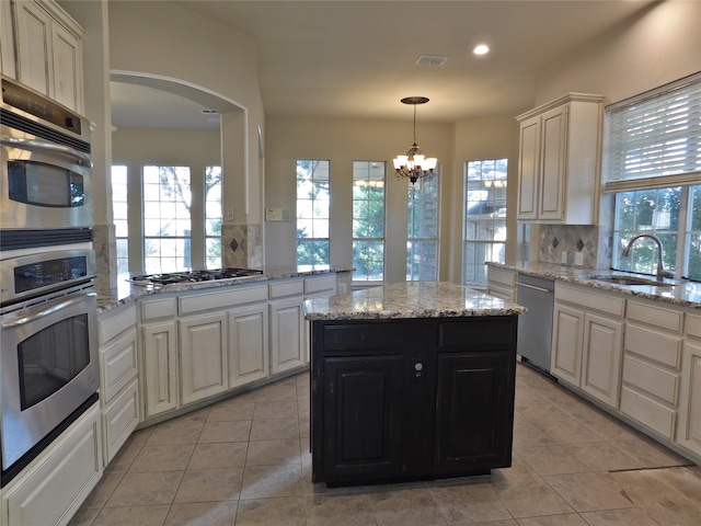 kitchen with decorative backsplash, appliances with stainless steel finishes, sink, a notable chandelier, and a center island