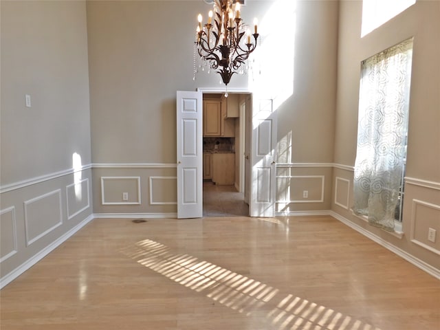 spare room featuring light hardwood / wood-style flooring, a chandelier, and a high ceiling