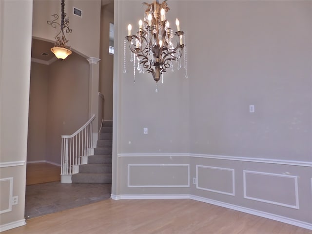 empty room featuring an inviting chandelier, ornate columns, and light wood-type flooring