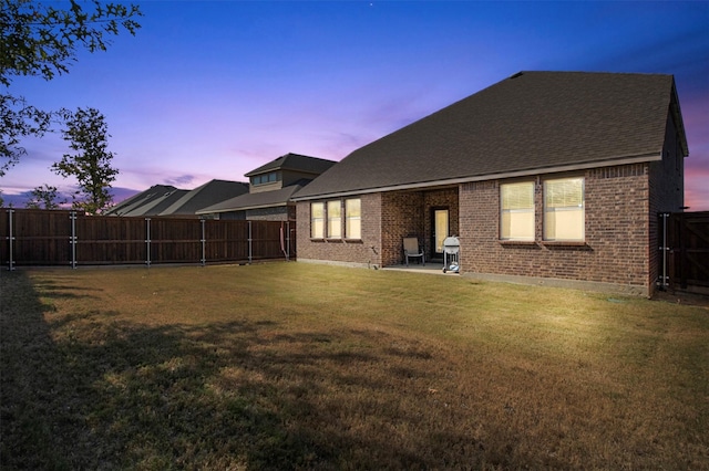 back house at dusk featuring a patio and a yard