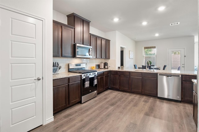 kitchen with appliances with stainless steel finishes, sink, backsplash, light stone counters, and light hardwood / wood-style floors