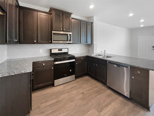 kitchen featuring kitchen peninsula, stainless steel appliances, sink, light wood-type flooring, and tasteful backsplash