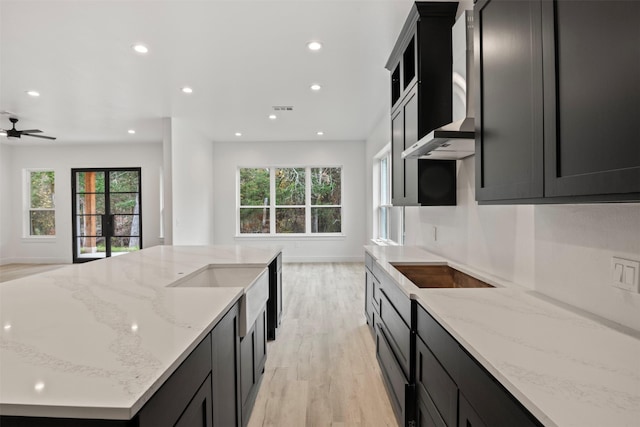 kitchen with black electric stovetop, wall chimney exhaust hood, light hardwood / wood-style floors, and light stone countertops