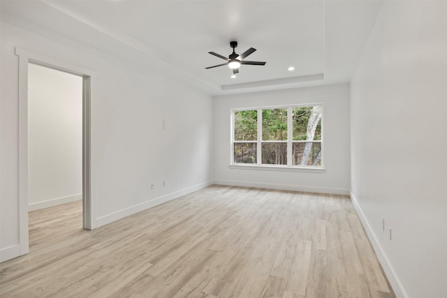 spare room featuring a raised ceiling, ceiling fan, and light hardwood / wood-style floors