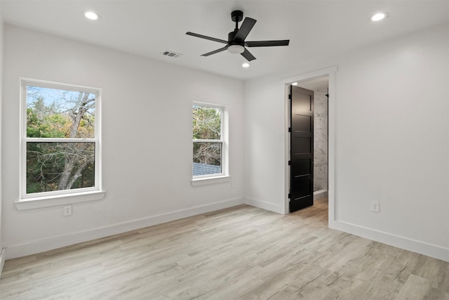 unfurnished bedroom featuring light wood-type flooring, ensuite bath, multiple windows, and ceiling fan