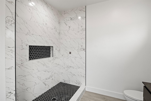 bathroom with a tile shower, hardwood / wood-style floors, vanity, and toilet