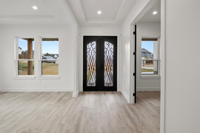 entryway with french doors, light hardwood / wood-style floors, a raised ceiling, and a wealth of natural light