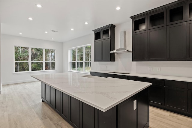 kitchen with light stone countertops, wall chimney range hood, light hardwood / wood-style flooring, stovetop, and a large island