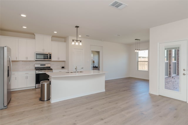 kitchen with stainless steel appliances, light hardwood / wood-style flooring, hanging light fixtures, and a kitchen island with sink