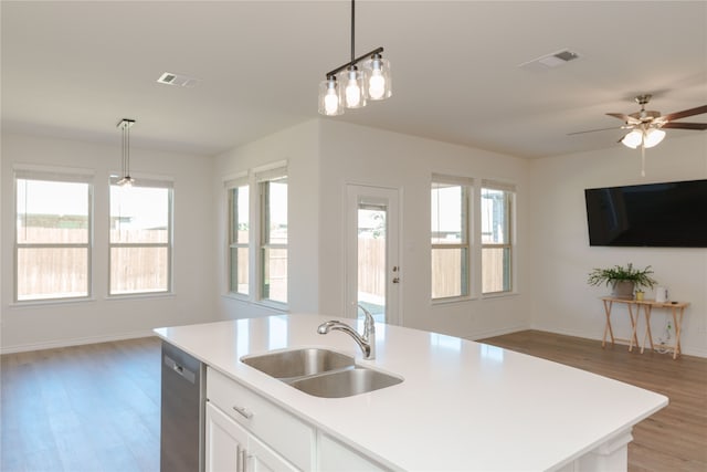 kitchen featuring a center island with sink, white cabinets, sink, light wood-type flooring, and decorative light fixtures