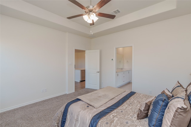 carpeted bedroom featuring a raised ceiling, ensuite bath, and ceiling fan