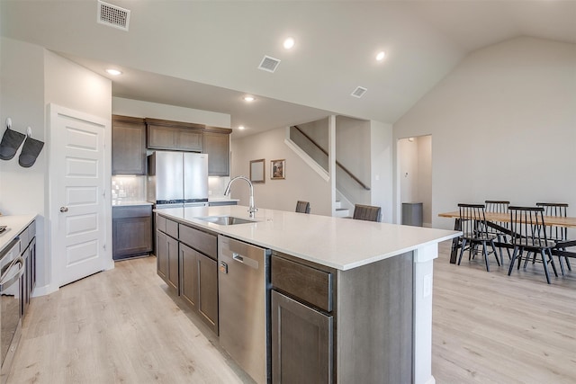 kitchen featuring an island with sink, light hardwood / wood-style flooring, stainless steel appliances, sink, and vaulted ceiling