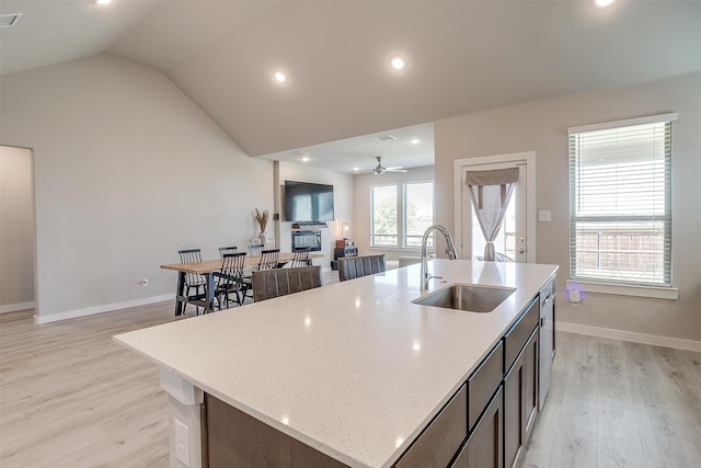 kitchen with light hardwood / wood-style flooring, a center island with sink, sink, vaulted ceiling, and ceiling fan