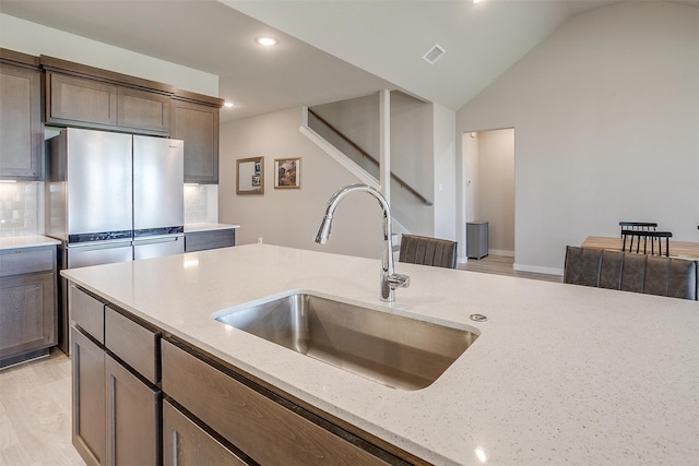 kitchen with light stone countertops, sink, light wood-type flooring, backsplash, and lofted ceiling