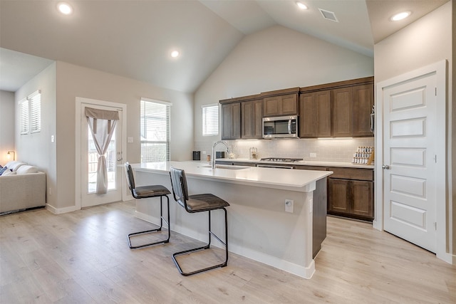 kitchen with stainless steel appliances, backsplash, a center island with sink, sink, and light hardwood / wood-style floors