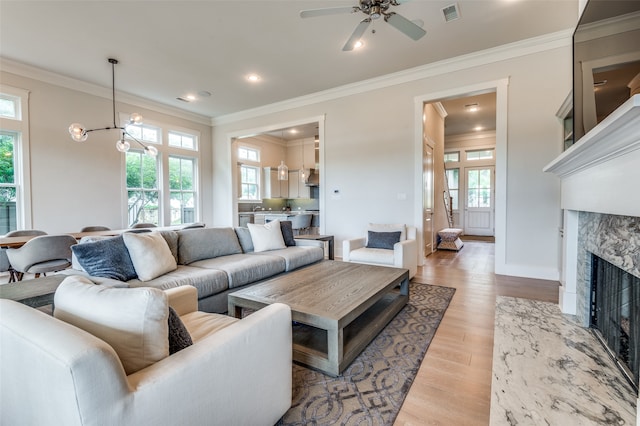 living room featuring light hardwood / wood-style flooring, ceiling fan with notable chandelier, a fireplace, and crown molding