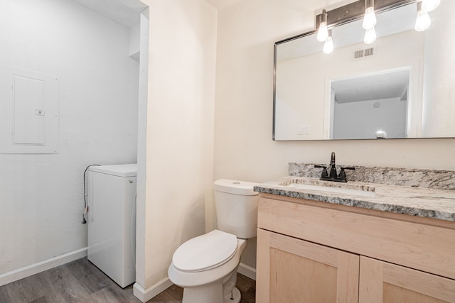 bathroom featuring toilet, washer / dryer, wood-type flooring, vanity, and electric panel