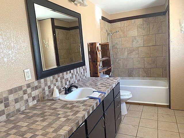 full bathroom with toilet, tile patterned floors, tiled shower / bath, vanity, and decorative backsplash