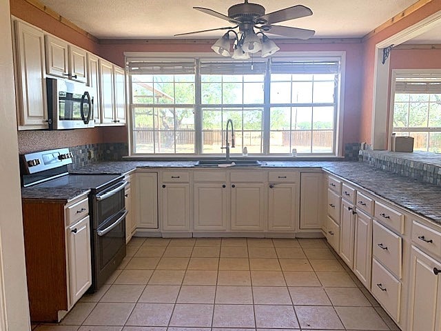 kitchen with white cabinets, light tile patterned floors, appliances with stainless steel finishes, ceiling fan, and sink