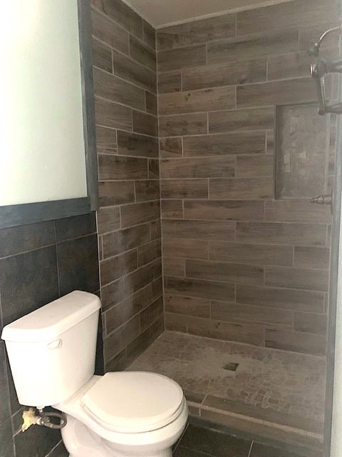 bathroom with tile walls, a tile shower, and toilet