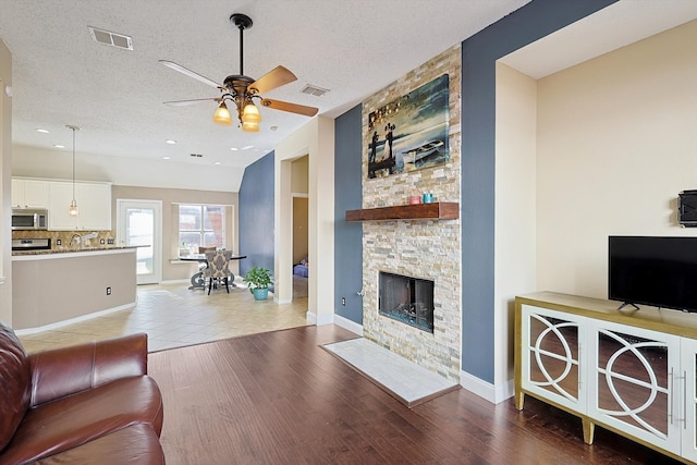 living room with ceiling fan, sink, hardwood / wood-style floors, a textured ceiling, and a fireplace