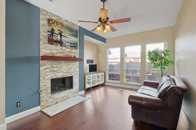 living room with dark hardwood / wood-style floors, ceiling fan, and a stone fireplace