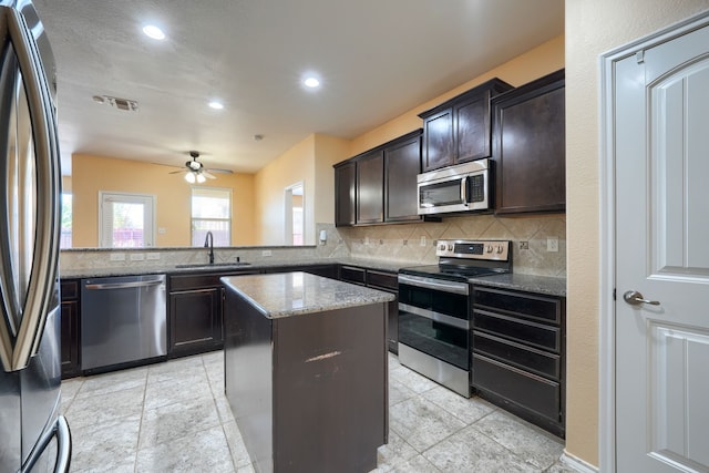 kitchen with kitchen peninsula, light stone counters, a kitchen island, sink, and stainless steel appliances